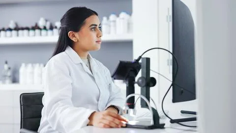 Young scientist using a computer and microscope in a lab. Female pathologist Stock Photos
