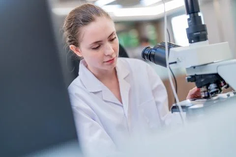 Young scientist working intently at a microscope in a modern laboratory set.. Stock Photos