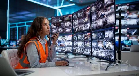 Young Security Guard Monitors Multiple CCTV Cameras In Busy Control Room. Stock Photos
