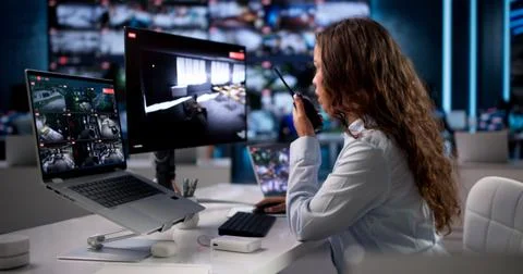 Young Security Guard Watching Multiple CCTV Cameras While Using Laptop In Con Stock Photos