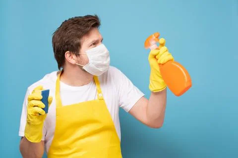 Young seious man in apron, protective mask and gloves ready to clean everything Stock Photos