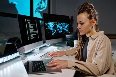 Young serious female programmer using laptop by workplace in office Stock Photos