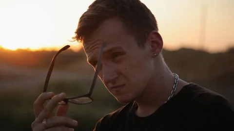 Young serious guy take off the glasses outdoors at sunset 1 Video stock 94442448