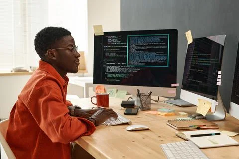 Young serious IT engineer in smart orange shirt looking at coded data Stock Photos