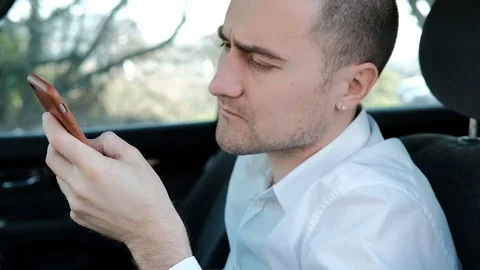 Young serious man with a beard sitting in the car and holds the phone Video stock 74317515