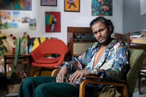 Young serious non-binary man in trendy clothes sitting in armchair Stock Photos