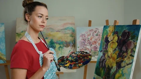 Young serious painter looking at her masterpiece and thinking what else to add Stock Footage 74197377