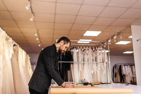 Young serious tailor with beard looking on drawing near wooden table with thr Fotos de archivo