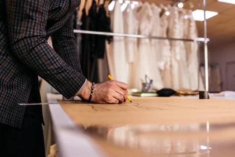 Young serious tailor with beard looking at drawing near wooden table with thr Stock Photos