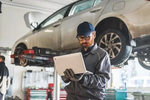 Young serviceman checking car diagnostics with a laptop, car in the background Stock Photos