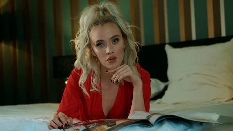 Young sexy blonde is lying on bed in bedroom with a magazine Stock Footage 101552031