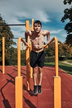 Young shirtless bodybuilder doing dips on parallel bars during his workout in 写真素材