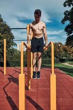 Young shirtless bodybuilder doing dips on parallel bars during his workout in Stock Photos