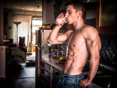 Young shirtless man in kitchen drinking water Stock-Fotos