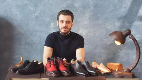 Young Shoe designer looking at the camera shows his work Stock Photos