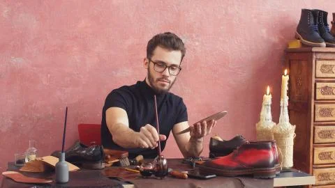 Young Shoe designer using a brush while working in shoe shop with modern Stock Photos