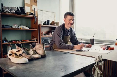 A young shoemaker makes a drawing for a pattern for leather shoes on a table in Stock Photos