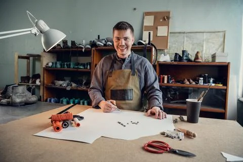 A young shoemaker makes a drawing for a pattern for leather shoes on a table in Foto stock
