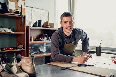A young shoemaker makes a drawing for a pattern for leather shoes on a table in Stock Photos