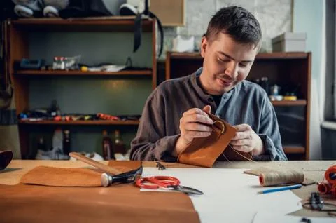 A young shoemaker manually sews decorative elements to leather shoes in the Stock Photos