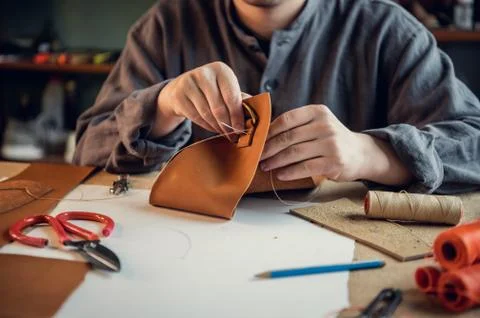 A young shoemaker manually sews decorative elements to leather shoes in the Stock Photos