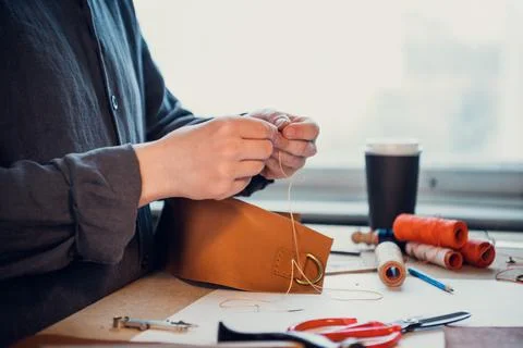 A young shoemaker manually sews decorative elements to leather shoes in the Stock Photos