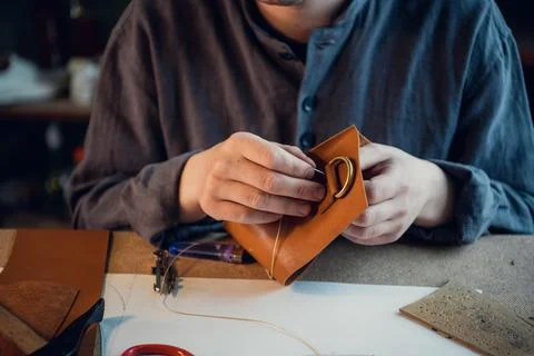 A young shoemaker manually sews decorative elements to leather shoes in the Stock Photos