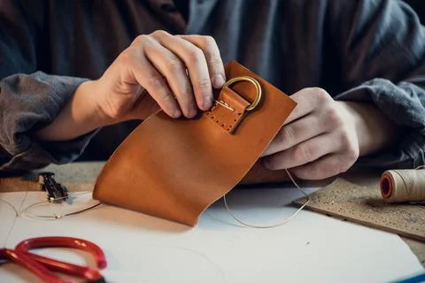 A young shoemaker manually sews decorative elements to leather shoes in the Stock Photos