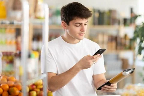 Young shopper using mobile app to pay for spaghetti in grocery store Fotos de archivo