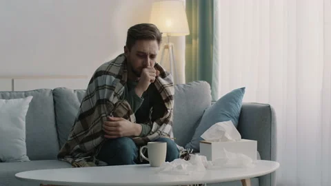 Young sick guy wrapped in plaid suffering from cough attack and drinking healing Stock Footage 151790295