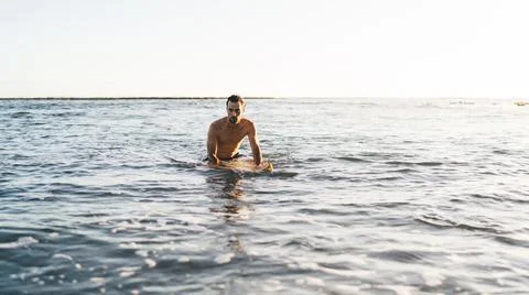 Young single guy sitting at professional surfboard surrounded by ocean water on Stock Photos