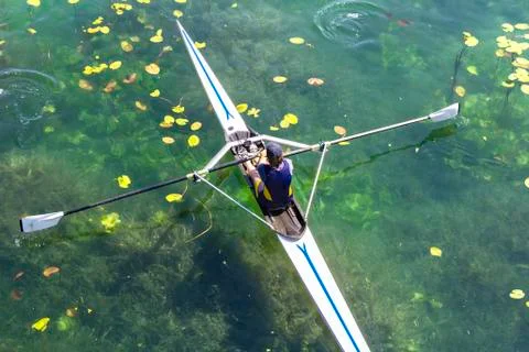 A Young single scull rowing competitor paddles on the tranquil lake Stock Photos