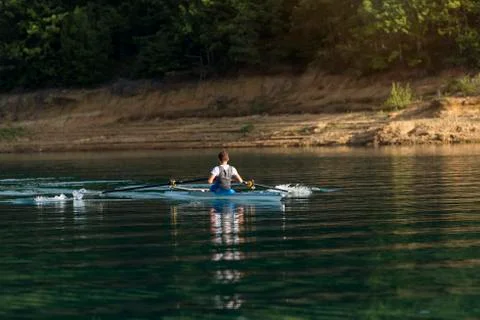 A Young single scull rowing competitor paddles on the tranquil lake Stock Photos