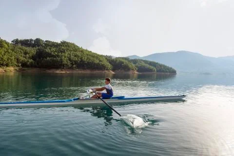 A Young single scull rowing competitor paddles on the tranquil lake Фото