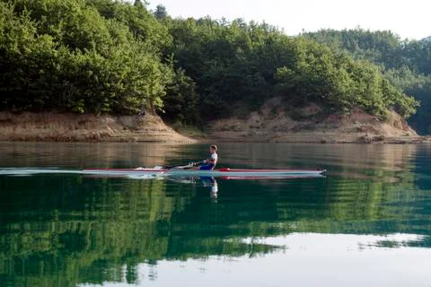 A Young single scull rowing competitor paddles on the tranquil lake Stock Photos