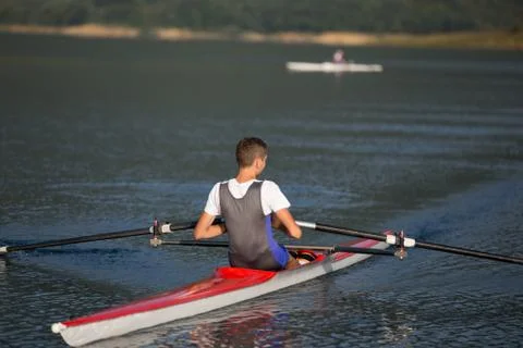 A Young single scull rowing competitor paddles on the tranquil lake 写真素材