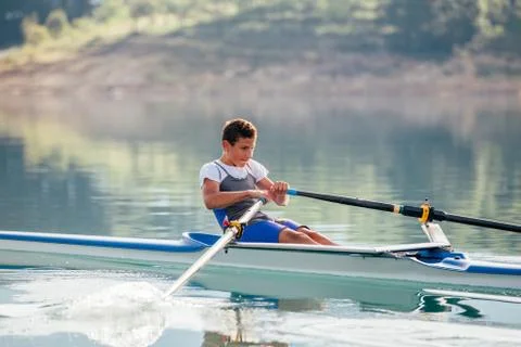 A Young single scull rowing competitor paddles on the tranquil lake Stock Photos
