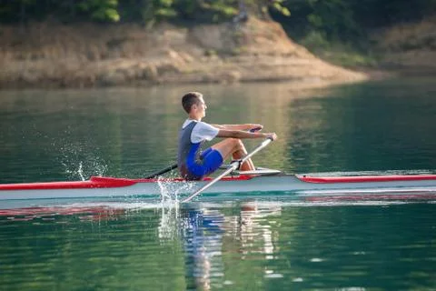 A Young single scull rowing competitor paddles on the tranquil lake Stock Photos