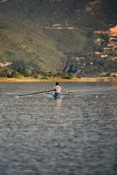 A Young single scull rowing competitor paddles on the tranquil lake Stock Photos