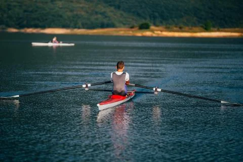 A Young single scull rowing competitor paddles on the tranquil lake Stock Photos