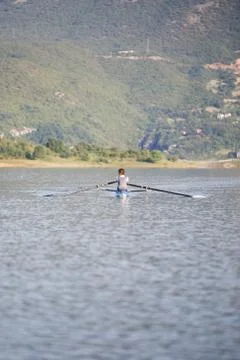 A Young single scull rowing competitor paddles on the tranquil lake Фото