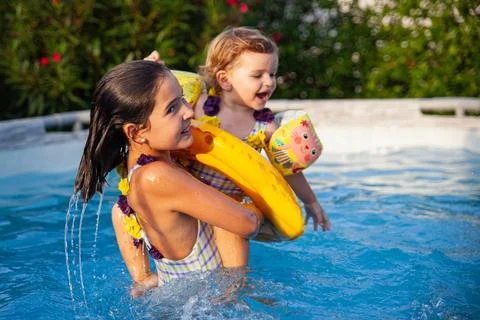 Young sisters with floatie enjoying pool play on sunny afternoon. Stock Photos