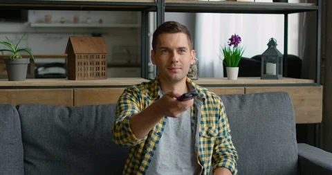 Young is sitting on a sofa and changing TV channels Stock Footage 113616551