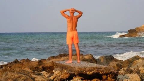 A young slender bald man in orange shorts and a naked torso stands Stock Footage 134828367