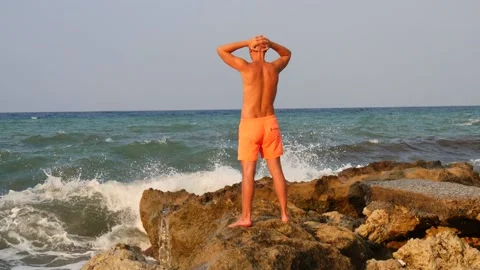 A young slender bald man in orange shorts and a naked torso stands Stock Footage 134833328