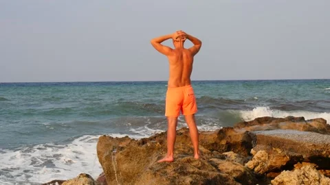A young slender bald man in orange shorts and a naked torso stands Stock Footage 134833509