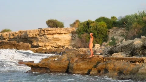 A young slender bald man in orange shorts and a naked torso stands Stock Footage 134834476