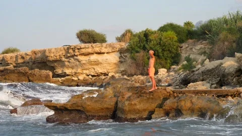 A young slender bald man in orange shorts and a naked torso stands Stock Footage 134836306