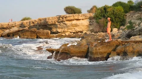 A young slender bald man in orange shorts and a naked torso stands Stock Footage 134837669