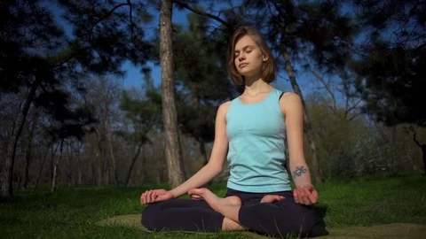 Young slim female sitting in lotus pose on lawn in park slow motion Stock Footage